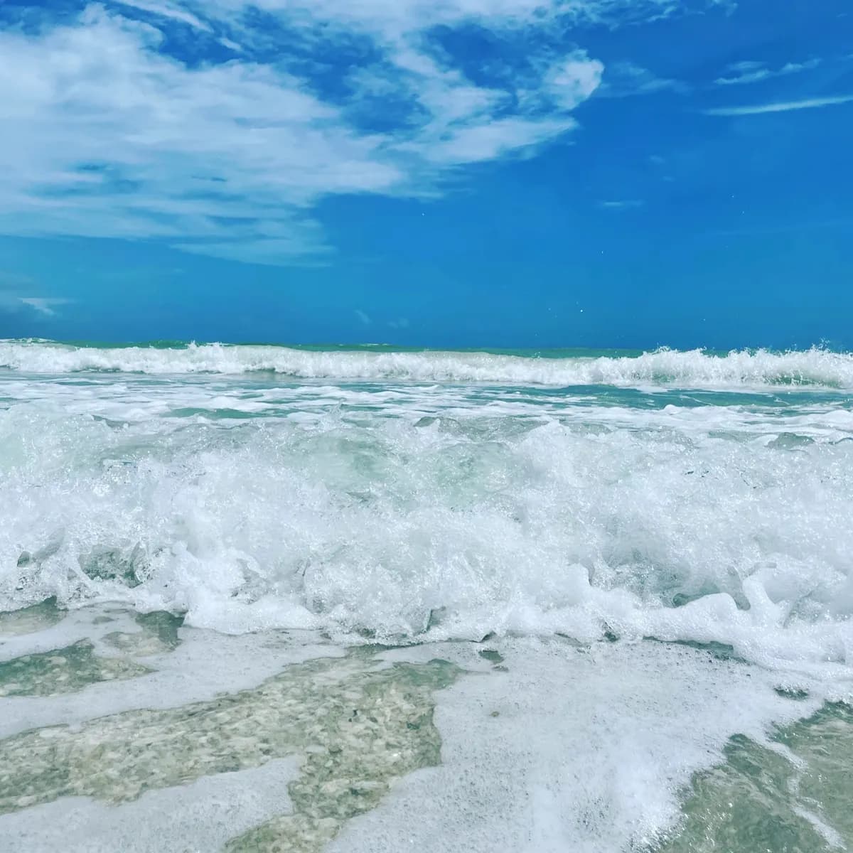Bright blue sky over Sanibel Island beach with foamy waves on white sand