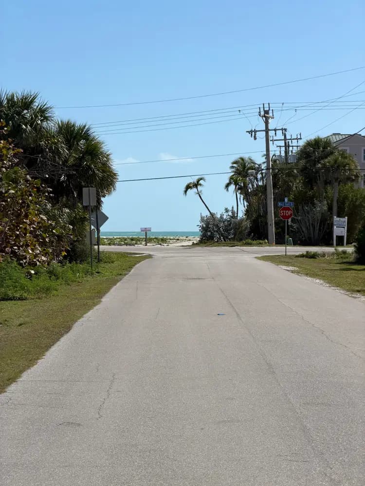Road leading to a sandy Sanibel Island beach with palm trees under blue sky